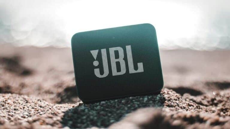 Caixa de som Bluetooth da marca JBL posicionada na areia da praia, usada como imagem destacada do artigo