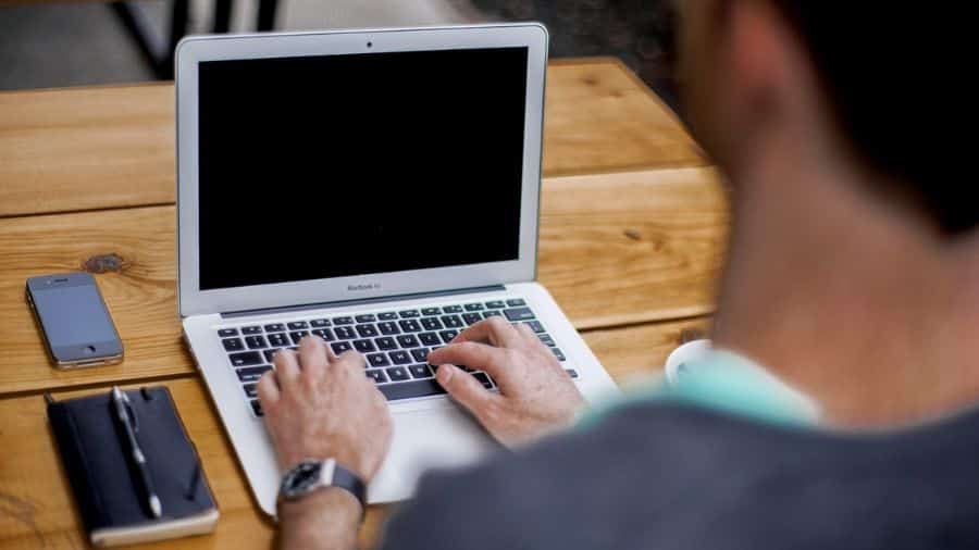 homem sentado em uma mesa configurando o seu Notebook