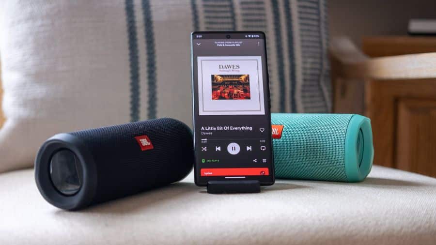 Imagem da caixa de som JBL portátil bluetooth ao lado de smartphone com música, ideal para uso em ambientes internos
